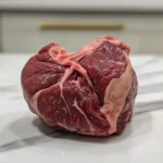 Close-up shot of fresh beef heart on white marble kitchen counter.